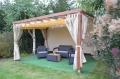 Custom waterproof garden curtains hanging on a wooden pergola with outdoor lounge furniture on a terrace.