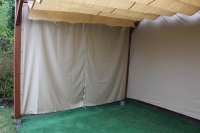 Custom-made waterproof outdoor curtains on a wooden garden gazebo structure with a green artificial grass floor.