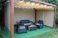 Custom-made HDPE Roman shade for a patio pergola with a brown wicker garden furniture set on green artificial grass.