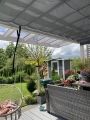Maßgeschneidertes graues horizontales Sonnenschutzrollo unter dem Glasdach einer modernen Gartenterrasse montiert