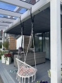 Tenda da sole orizzontale grigia sotto la copertura del terrazzo in travi bianche con poltrona sospesa e mobili da giardino