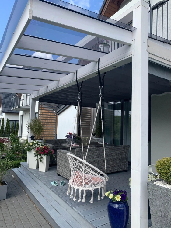Grijs horizontaal zonnescherm onder een glazen overkapping op een modern terras met tuinmeubilair