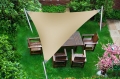 Triangle waterproof PVC sun shade sail installed over a wooden garden dining set in a lush green backyard.