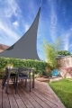 Vela ombreggiante triangolare grigia in HDPE montata sopra un terrazzo con mobili da giardino e piante