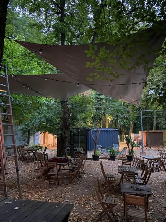 Custom-sized waterproof triangular PVC sun shade sails hanging over an outdoor cafe patio in a wooded area