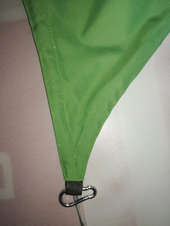 Corner detail of a green triangular waterproof sun shade sail with a webbing loop and metal carabiner attachment
