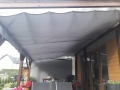 Graues wasserdichtes ausziehbares Sonnensegel 3x3 m montiert auf einer Holzpergola über der Freizeitterrasse