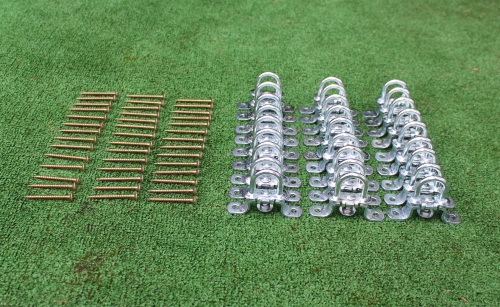 Set of silver metal D-ring mounting brackets and gold wood screws for a PVC terrace canopy installation on green turf