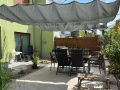 Vela ombreggiante grigia impermeabile retrattile su misura montata su una terrazza con mobili da giardino e piante