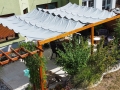 Tenda a vela grigia impermeabile e scorrevole montata su un pergolato in legno in giardino sopra un set di mobili da esterno