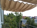 Vela ombreggiante scorrevole impermeabile su misura montata su una terrazza con vista sulla città e sugli alberi