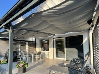Vodotesná, výsuvná záhradná slnečná clona v sivej farbe inštalovaná pod zastrešením terasy