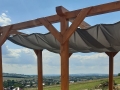 Graues wasserdichtes Sonnensegel 3x3 m montiert unter einer Holzpergola vor einer Landschaft