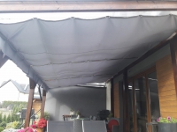 Retractable grey waterproof sun shade sail installed over a wooden pergola on a modern patio terrace landscape