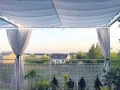 Weißes ausziehbares wasserdichtes Sonnensegel 2,5x4 m auf einer Terrasse mit weißen Vorhängen und Blick auf Häuser