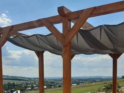 Retractable waterproof sun sail shade on a wooden pergola overlooking a scenic valley landscape.