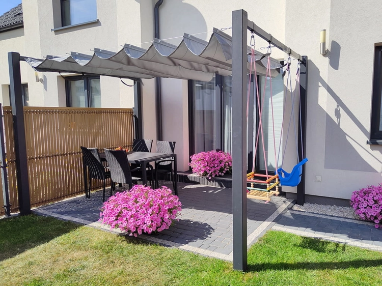 Grey retractable roman terrace canopy installed over a modern patio with dining furniture and children's swings