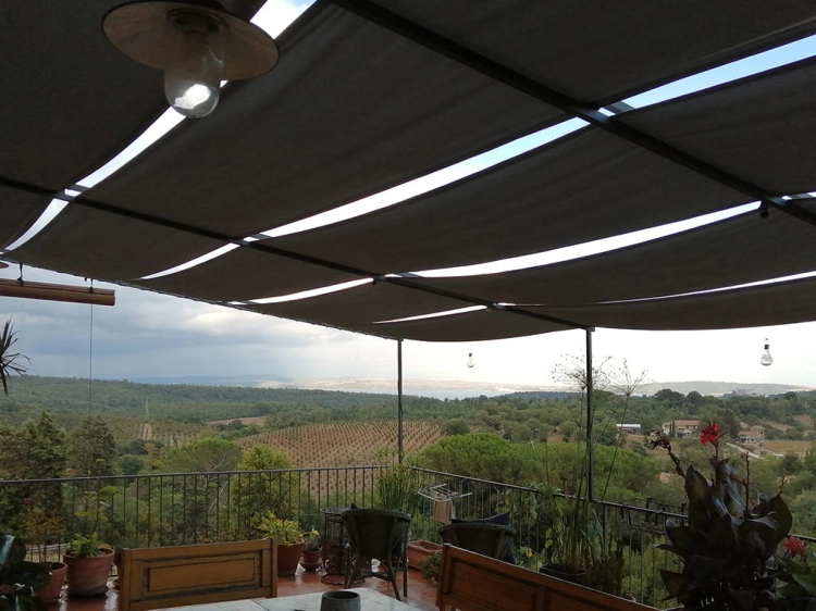 Waterproof sunshade canopy installed on a terrace pergola overlooking a scenic valley with hills and vineyards.
