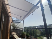 Weißes Sonnensegel nach Maß über einer Terrasse mit Loungemöbeln und Lichterkette montiert
