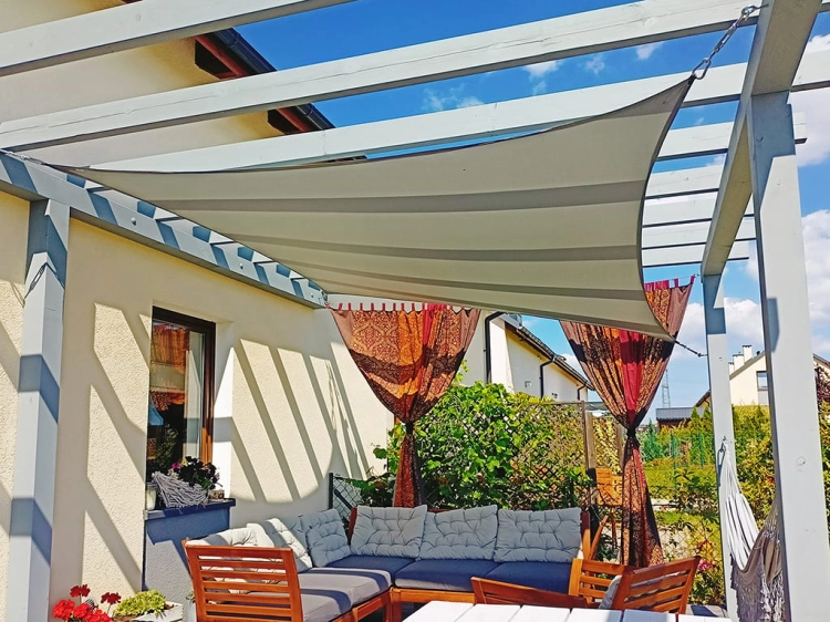 Waterproof garden sun sail shade installed over a patio lounge area with a wooden pergola and outdoor furniture