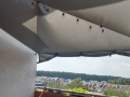 Graues Sonnensegel wasserdicht 3x4 m auf dem Balkon montiert, dekoriert mit einer Lichterkette aus Glühbirnen.
