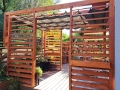 Modern wooden pergola with a grey HDPE retractable wave shade sail installed on a backyard terrace deck.
