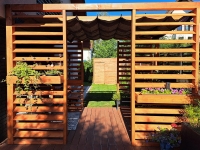 Custom retractable HDPE shade sail under a timber patio pergola with horizontal wooden slats and flower boxes