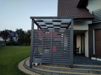 Custom-sized sunshade sail fabric strips woven through a wooden pergola over a stone patio next to a house.