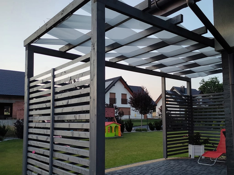 Custom retractable sunshade fabric strips woven through a modern grey wooden garden pergola over a stone patio