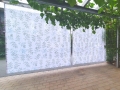 Floral patterned garden curtains hanging from a pergola over a paved patio area.