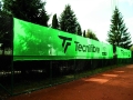 Green Tecnifibre tennis court windbreak screen and privacy banner mounted on a fence next to a clay court