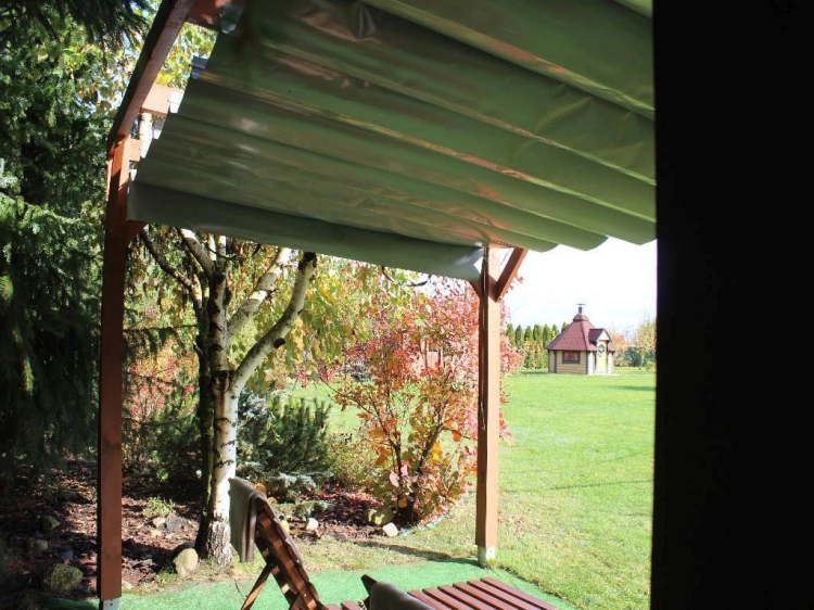Hellgraues Raffrollo auf einer Terrasse mit Holzkonstruktion und Seilzugsystem zum Ausfahren des Stoffes