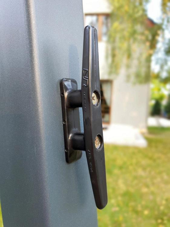 Schwarze Schnurklemme an einem graphitfarbenen Profil, Element des Seilzugsystems für Raffrollos