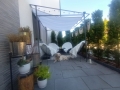Vela ombreggiante scorrevole bianca impermeabile su pergola in metallo sopra una terrazza con mobili e un cane