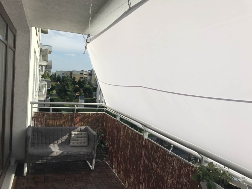 Custom-sized waterproof white sun shade sail installed on a residential balcony above a lounge sofa and wooden flooring.