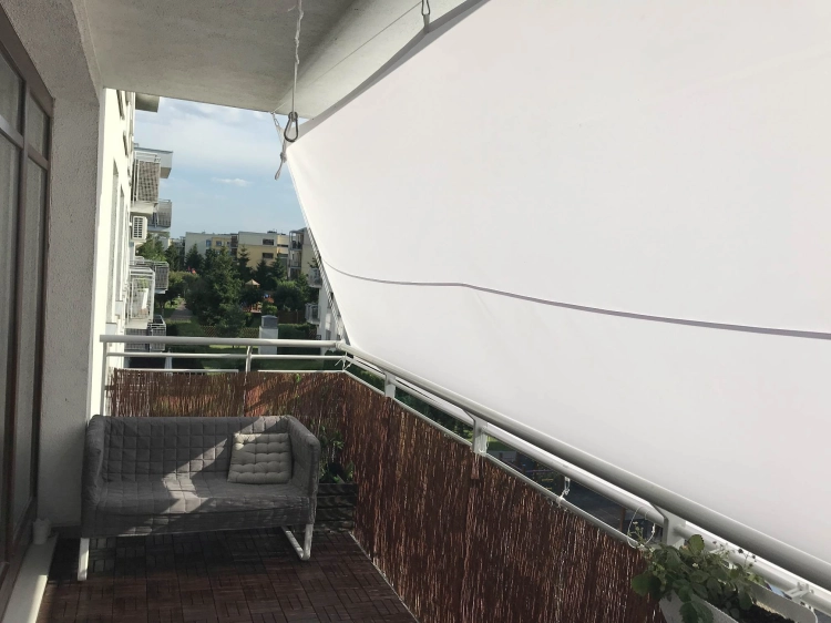 Custom-sized waterproof white sun shade sail installed on a residential balcony above a lounge sofa and wooden flooring.