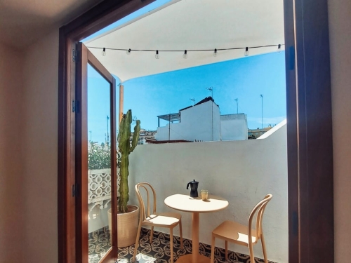 White waterproof balcony shade sail over a patio with a table, chairs, cafe moka pot, and a cactus in a pot