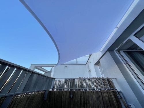 White waterproof custom-sized sun sail shade installed over a modern balcony for UV protection and privacy
