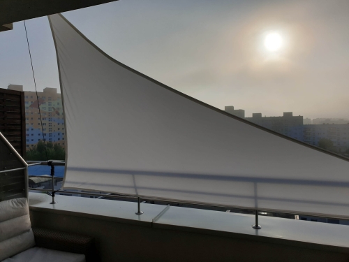White waterproof triangular sun shade sail installed on a city balcony for UV protection and privacy