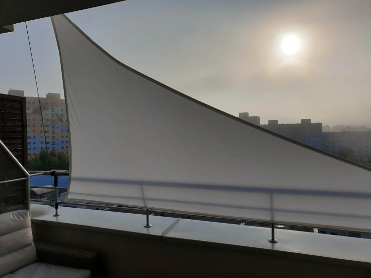 White waterproof triangular sun shade sail installed on a city balcony for UV protection and privacy