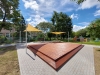 Yellow triangular HDPE shade sail over a wooden garden platform with playground equipment in the background
