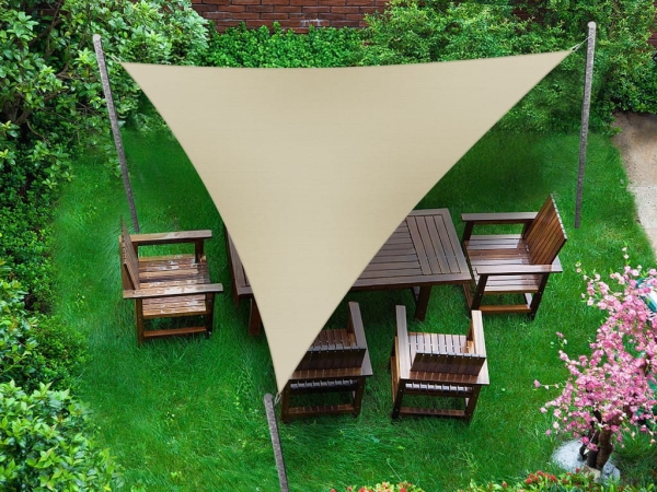 Beige triangular waterproof sun shade sail over a wooden garden dining set on a green lawn.