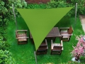 Grünes dreieckiges Sonnensegel über einem Gartenmöbel-Set aus Holz auf dem Rasen