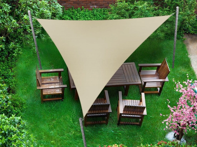 Trojuholníková béžová tieniaca plachta 5,2 m natiahnutá nad dreveným záhradným nábytkom na zelenom trávniku