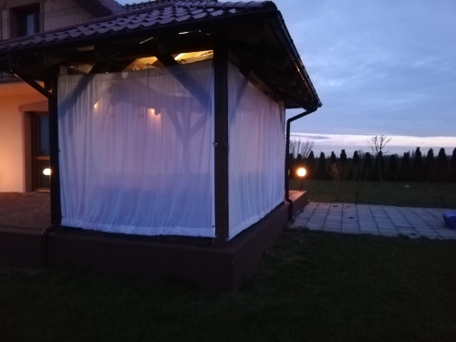 Weiße Terrassenvorhang aus Voile schirmt einen beleuchteten Gartenpavillon in der Dämmerung ab
