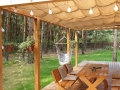 Beigefarbenes wasserdichtes Sonnensegel ausziehbar 3x3 m montiert an einer Holzpergola über der Terrasse mit Loungemöbeln