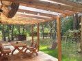 Beiges wasserdichtes ausziehbares Sonnensegel montiert unter der Überdachung einer Holzterrasse mit Lounge-Möbeln