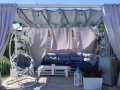 Wasserdichtes ausziehbares Sonnensegel Premium 3x5 m montiert an einer weißen Pergola über einer Terrasse mit Palettenmöbeln