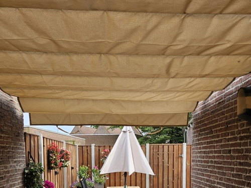 Beige 3x4 m premium waterproof roman blind for patio providing shade over a garden terrace with flowers and umbrella