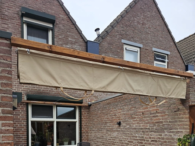 Tan waterproof premium roman blind for a 3x4 m terrace installed under a wooden beam on a brick house wall